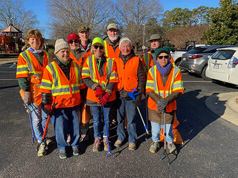 nine volunteers wearing orange vests and holding litter grabbers
