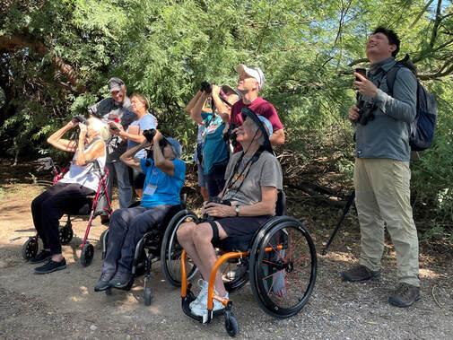 group of 8 people birdwatching, with some standing and some in wheelchairs 
